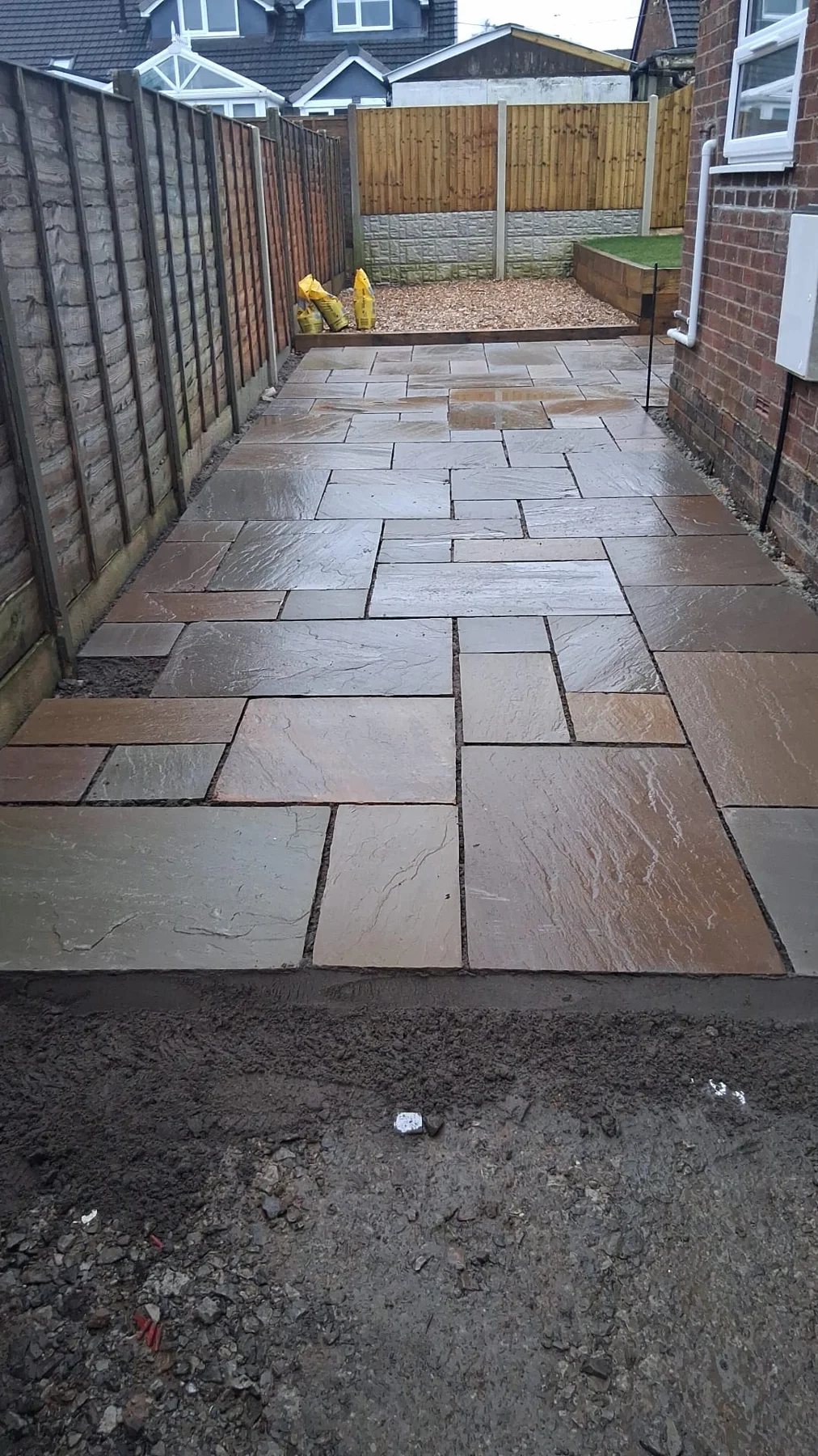 Stone-paved side path between timber fencing and a brick house