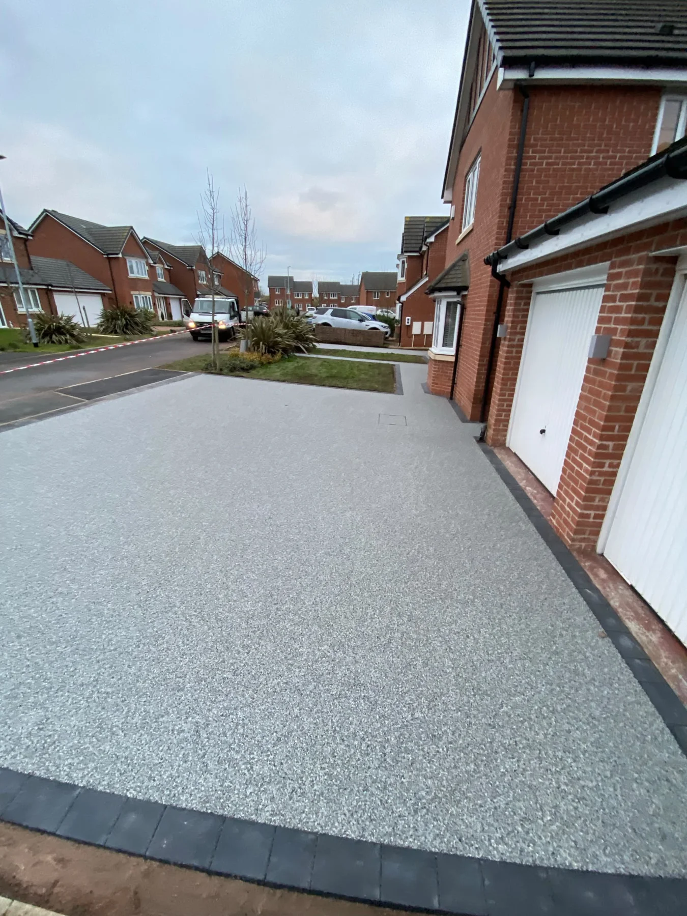 Pale resin driveway with dark edging beside a red-brick house — view 1