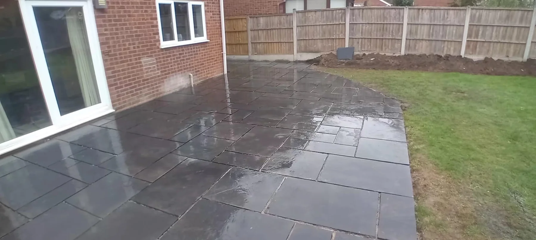 Dark stone patio beside a lawn and timber fencing — view 1