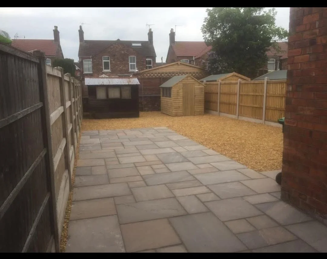 Paved seating area leading to a gravel garden and timber sheds