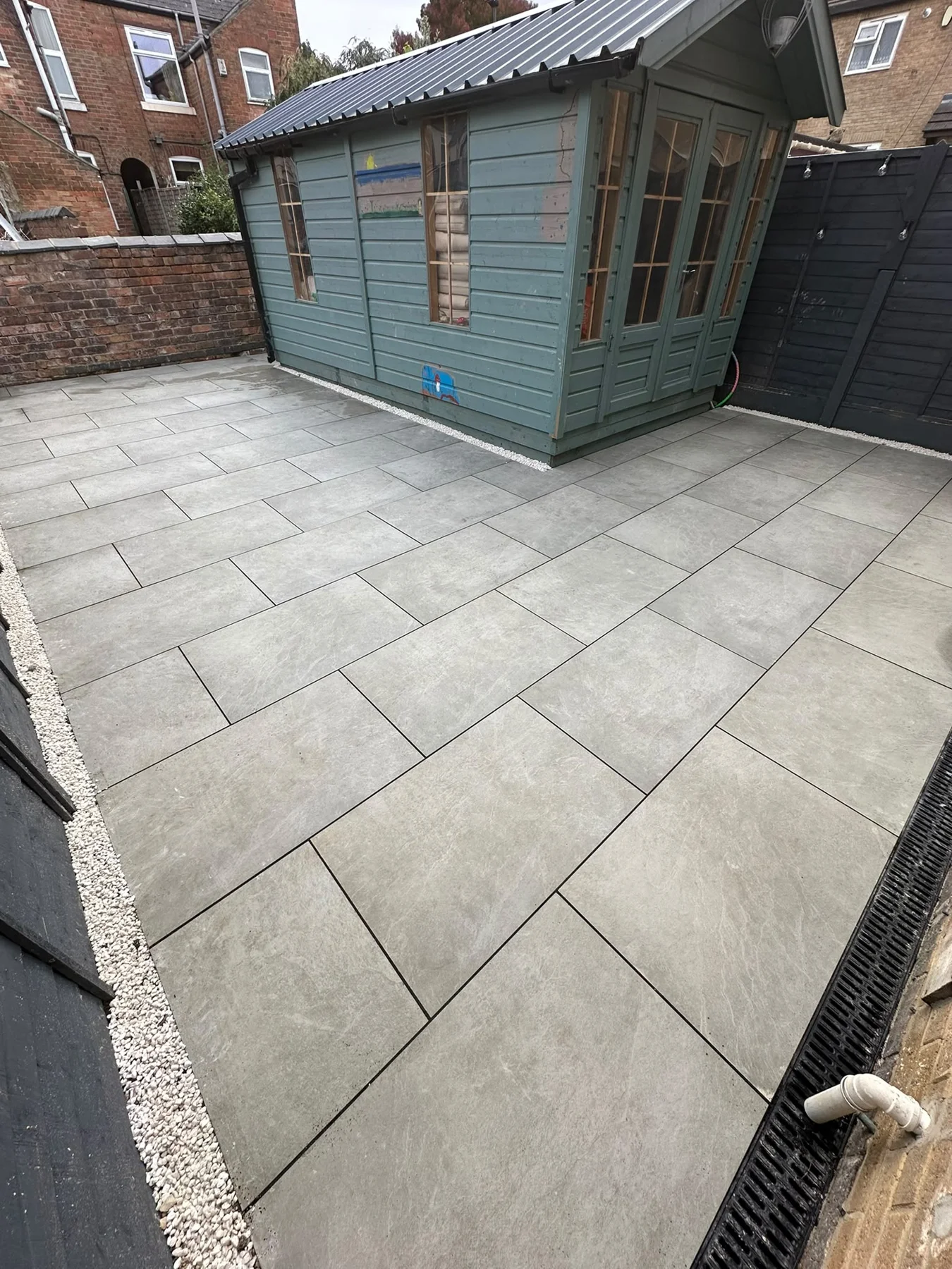 Grey paving around a green summerhouse beside a brick house — view 1
