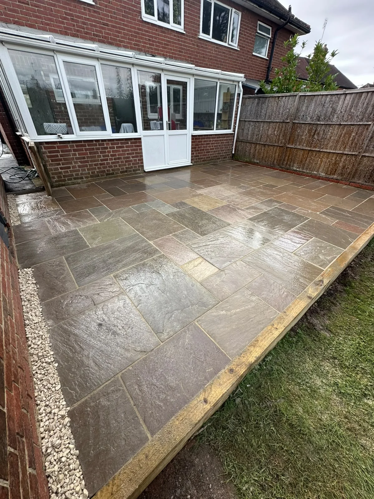 Stone patio beside a conservatory, with lawn and planting — view 1