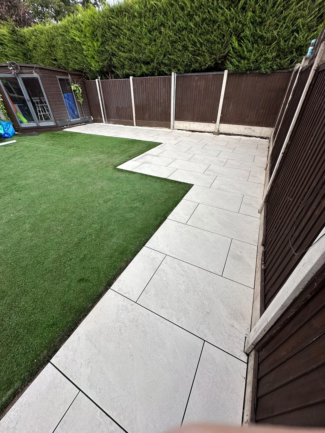 Light paving surrounding a rectangular lawn in a fenced garden — view 1